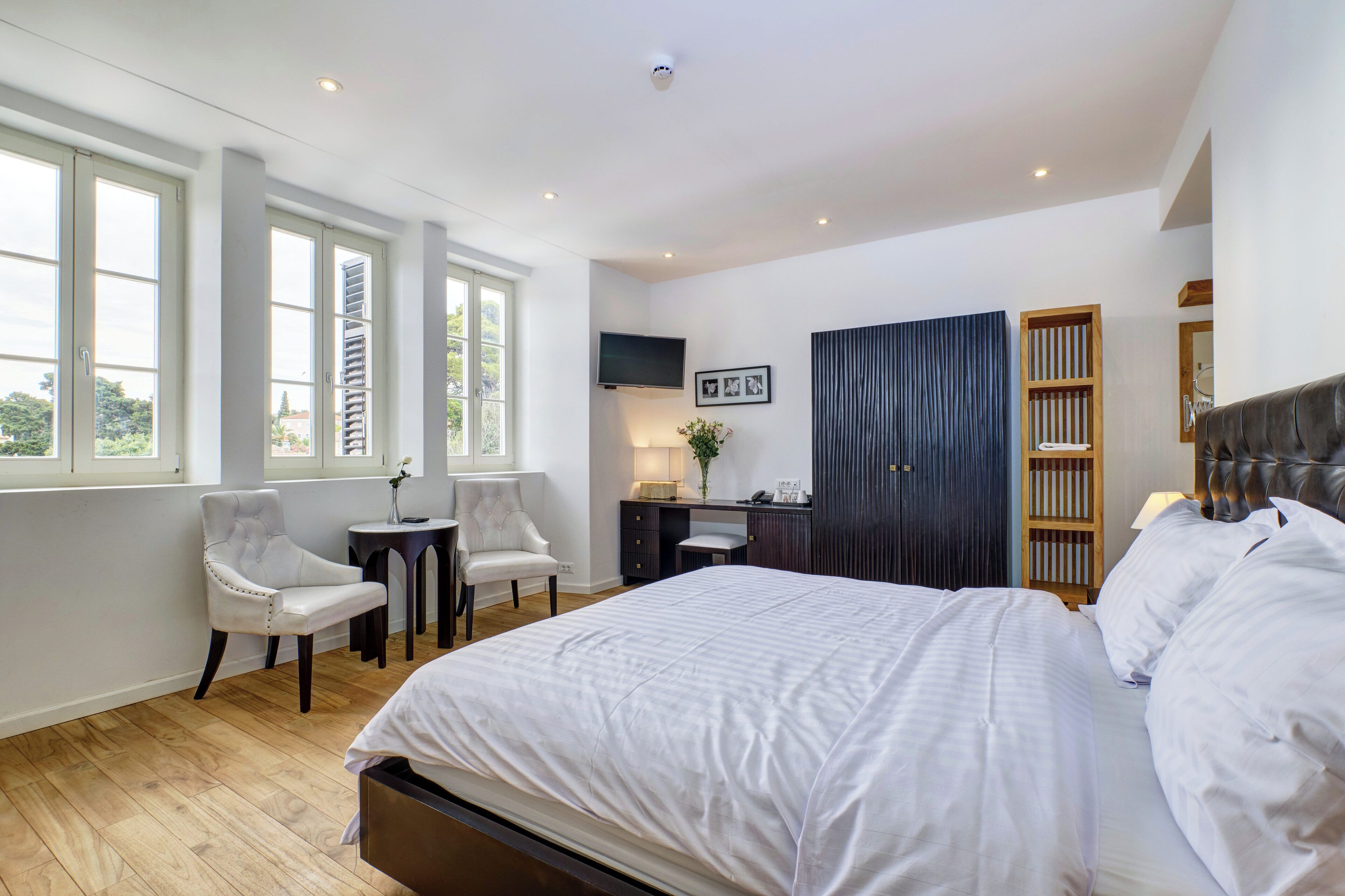 A bedroom with a large bed, a desk, two chairs, a TV, and a wardrobe.