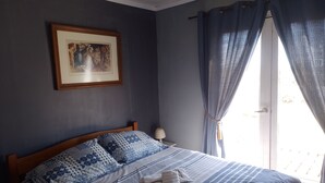 Una cama bien hecha con almohadas estampadas y una colcha a rayas, un cuadro en la pared y una ventana con cortinas.