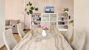 Ein Esszimmer mit einem Marmortisch, sechseckigen Stühlen, einer weißen Vase mit Blumen und einem Bücherregal mit diversen Gegenständen.