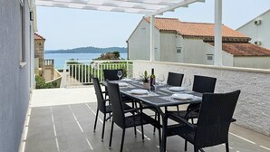 Eine Außenpatio mit Esstisch, mit Blick auf eine malerische Aussicht auf Meer und Hügel.