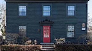 Une maison à deux étages avec une porte rouge, une cheminée et un petit porche.