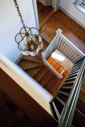 Un escalier en bois avec une rampe blanche, un petit banc blanc à sa base et un luminaire suspendu.