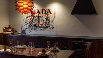 Ein Restaurantinnenraum mit einem für vier Personen gedeckten Esstisch, einer modernen Pendelleuchte und einer Wand mit einem großen abstrakten Gemälde.