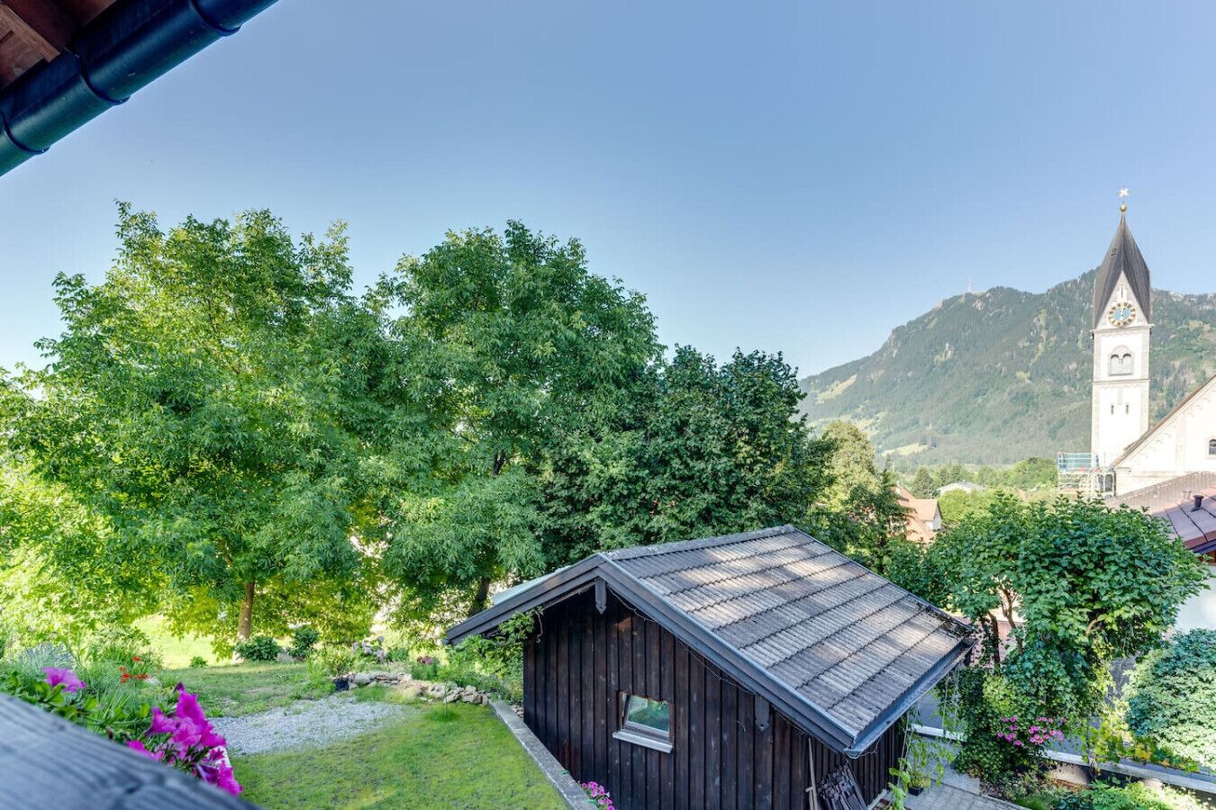 Une cabane en bois rustique, dotée d’un toit en pente, entourée d’une végétation luxuriante et avec une chaîne de montagnes en toile de fond.