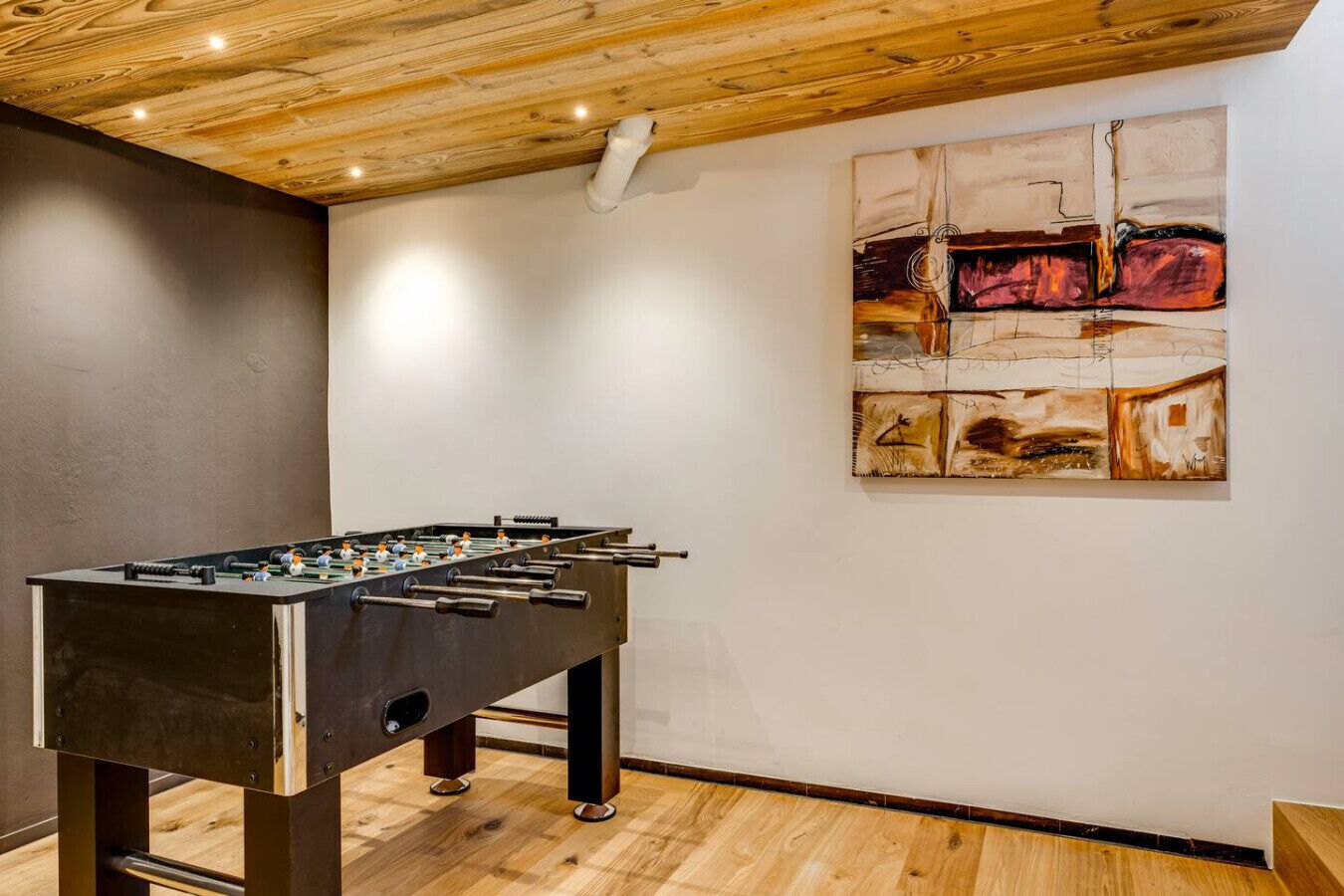 Een kamer met een tafelvoetbaltafel, houten plafond en abstracte kunst aan de muur.