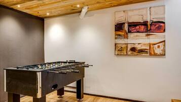 Een kamer met een tafelvoetbaltafel, houten plafond en abstracte kunst aan de muur.