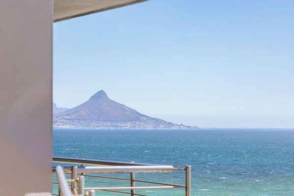 A coastal view with a mountain in the distance, a railing in the foreground, and a clear sky.