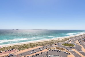 A coastal road with vehicles, a beach, and a clear sky.