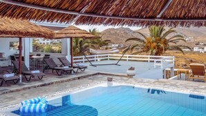A pool area with lounge chairs, a thatched umbrella, and a view of the landscape.