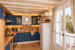 A kitchen with blue cabinets, a white refrigerator, and a window with curtains.