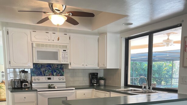 A modern kitchen with white cabinetry, a central island with stools, a microwave, stove, and coffee maker. - Palms and Paradise 3-bedroom 2-bath house with heated pool in serene Cape Coral. (Cape Coral)