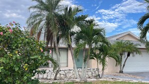 A residential area with a house featuring a stone wall, palm trees, and a garage. - Palms and Paradise 3-bedroom 2-bath house with heated pool in serene Cape Coral. (Cape Coral)
