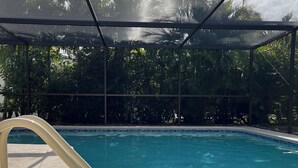 A clear swimming pool with a safety railing, surrounded by lush greenery and a covered area. - Palms and Paradise 3-bedroom 2-bath house with heated pool in serene Cape Coral. (Cape Coral)