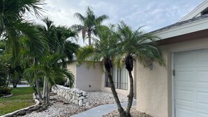 A residential area with palm trees, a stone wall, and a garage door. - Palms and Paradise 3-bedroom 2-bath house with heated pool in serene Cape Coral. (Cape Coral)