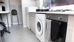 A compact kitchen with a washing machine, a sink, and a chair. - 2 Bedroom House - Sleeps 4 - Free Parking, Wifi (Leicester)