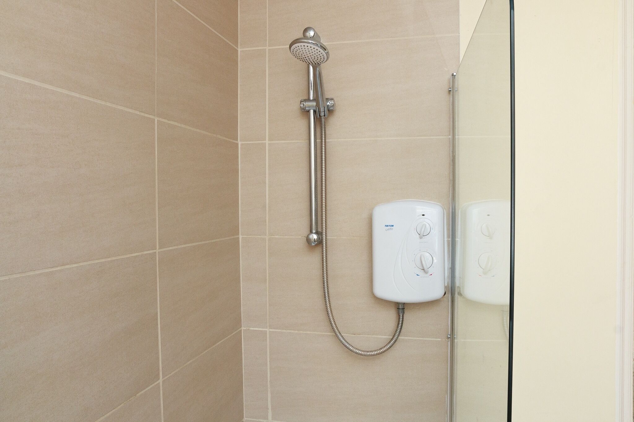 A shower with a handheld showerhead and a wall-mounted control panel.