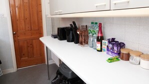 A kitchen with a wooden door, white cabinets, a countertop with various items including a bottle of water, a bottle of wine, and packaged food items. - 2 Bedroom House - Sleeps 4 - Free Parking, Wifi (Leicester)