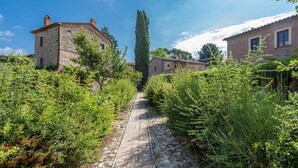 Un camino de piedra que conduce a edificios de piedra tradicionales rodeados de abundante vegetación.