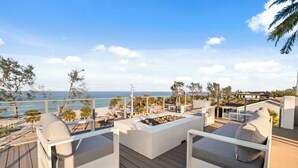 A deck with white furniture, a fire pit, and a view of the ocean.