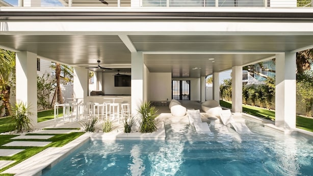 A modern outdoor pool area with a covered seating area and a view of the surrounding landscape.
