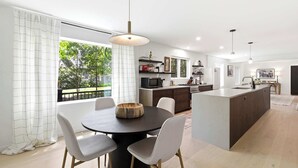 Una cocina moderna con una isla central, comedor con sillas y un amplio ventanal con cortinas.