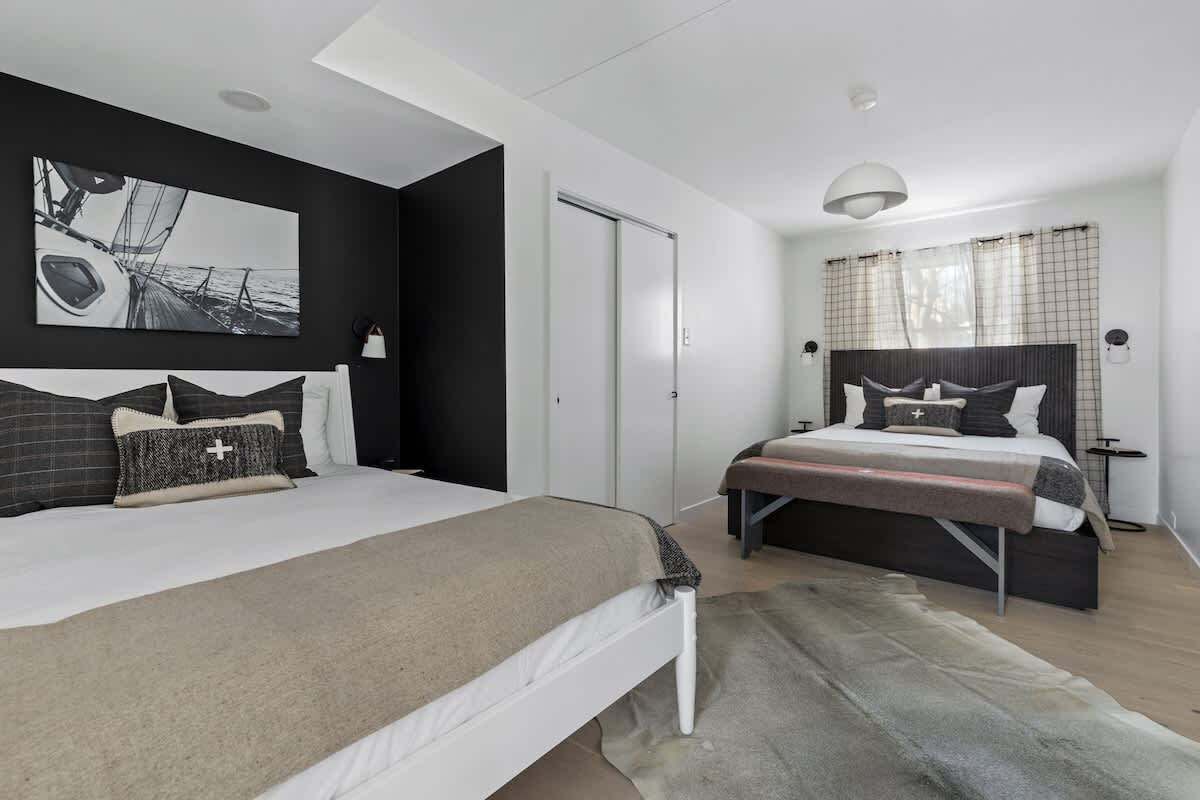 A modern bedroom with a large bed, a smaller bed, a painting, a wardrobe, and a window with curtains.