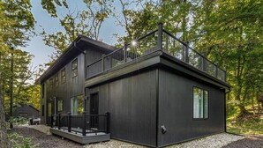 Una casa moderna de dos pisos con un balcón, rodeada de árboles.
