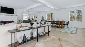 Una sala de estar moderna con chimenea, un comedor con sillas y un ventanal grande.