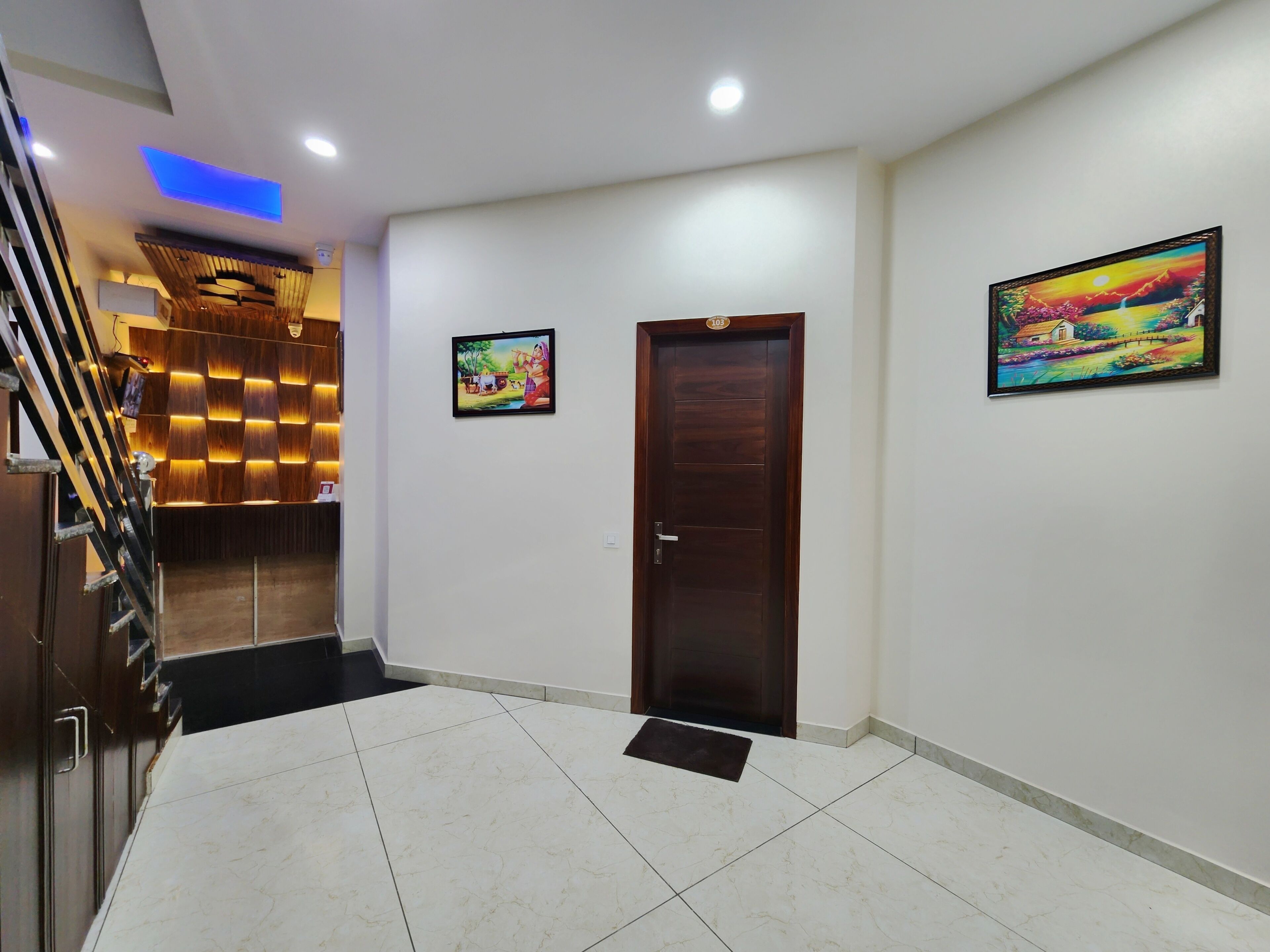 A hotel lobby with a wooden reception desk, a staircase, and two framed paintings on the walls.