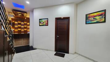 A hotel lobby with a wooden reception desk, a staircase, and two framed paintings on the walls.
