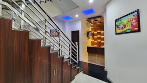 A staircase with wooden steps and metal railings, leading to a reception area with a wooden panel wall and a framed picture. - Raina's BnB (Solan)