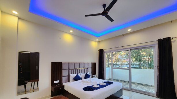 A modern bedroom with a large bed, a ceiling fan, and a view of the outdoors through a sliding glass door. - Raina's BnB (Solan)