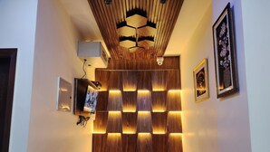 A reception area with a wooden panel wall, a red cushioned seating area, a mounted television, and framed artwork on the walls. - Raina's BnB (Solan)