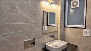 A modern bathroom with a white sink, a mirror, a wall-mounted light, and a window with a fan.