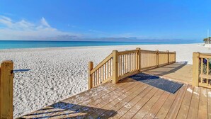 A wooden deck leading to a sandy beach with a clear blue sky.