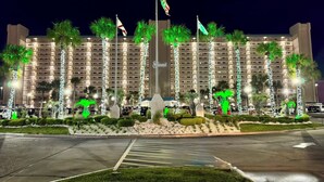 A hotel with a central flagpole, multiple flags, and a well-maintained garden with palm trees.