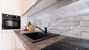 A modern kitchen with a black sink, white cabinets, and a brick-patterned backsplash. - Central 1-bedroom Apartment (Plovdiv)