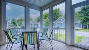 Un porche cubierto con una mesa y sillas, ventanas amplias y vista a casas vecinas.