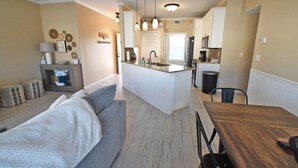 Una cocina moderna con una isla central, un comedor con mesa de madera y una sala de estar con sofá y televisor.