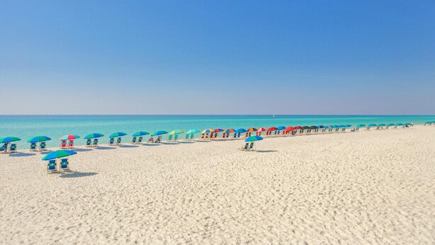 Una playa con hileras de sillas y sombrillas bajo un cielo despejado.