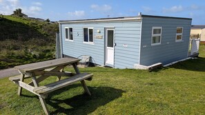 Une petite maison mobile bleu clair, dotée d’une porte, de fenêtres et d’une table de pique-nique devant.