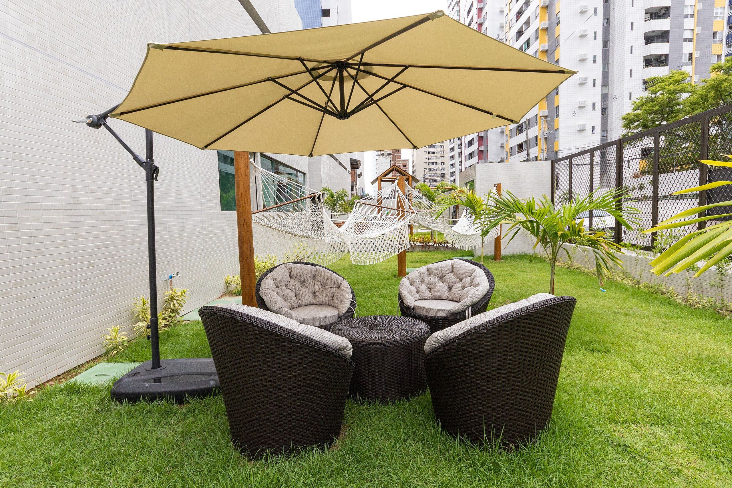 Un patio con mobiliario de mimbre, una hamaca y un paraguas grande.