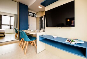 A modern kitchen with a dining area, a refrigerator, a flat-screen TV, and a window with a view. - Allure Boa Viagem por Carpediem (Recife)