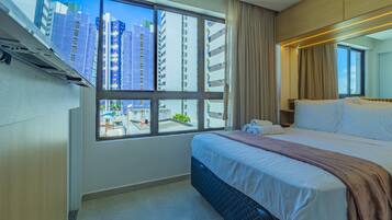 Habitación de hotel con un ventanal grande, una cama, una mesita de noche y vistas a edificios altos.