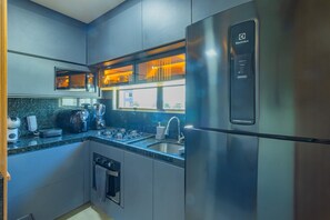 A modern kitchen with stainless steel appliances, a built-in oven, and a window above the sink. - Allure Boa Viagem por Carpediem (Recife)