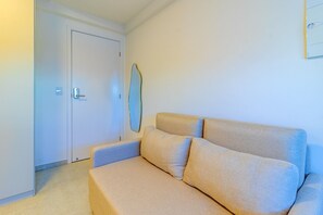 A room with a beige sofa, a white door, and a wall-mounted mirror. - Allure Boa Viagem por Carpediem (Recife)
