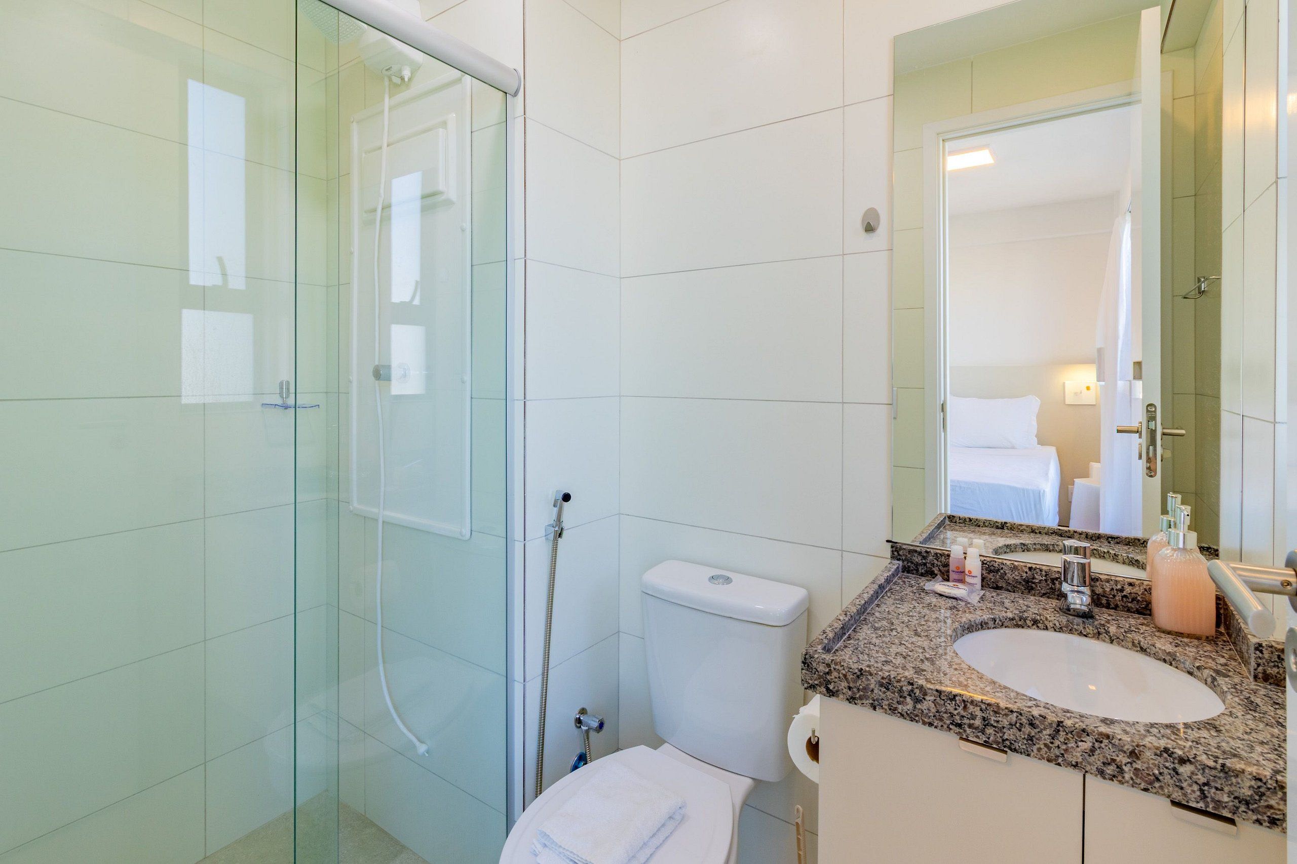 A modern bathroom with a glass shower enclosure, a white toilet, and a granite countertop sink.