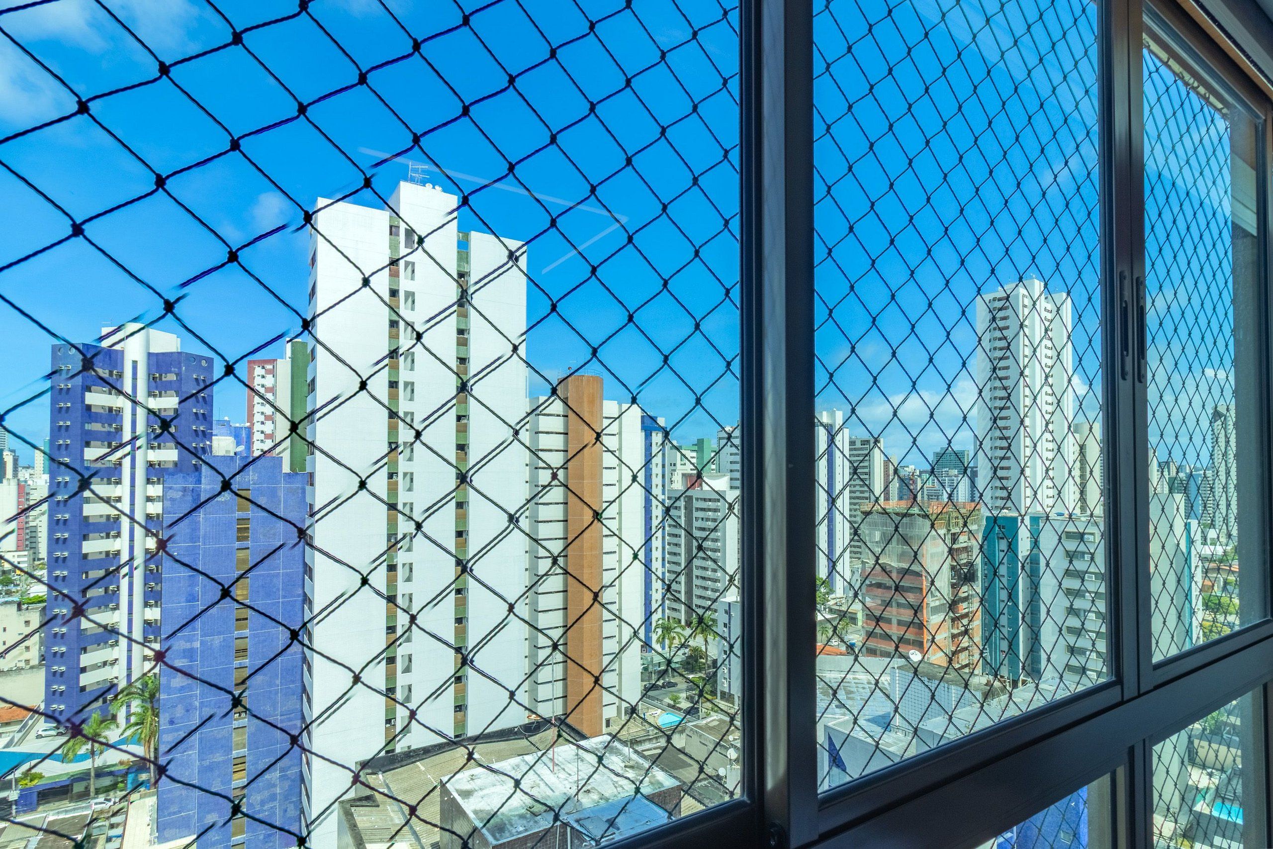 Visão da cidade através de uma cerca de arame, com edifícios altos ao fundo.
