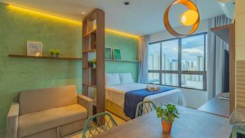 Quarto de hotel moderno com cama, sofá, mesa de jantar e uma grande janela com vista para a cidade.