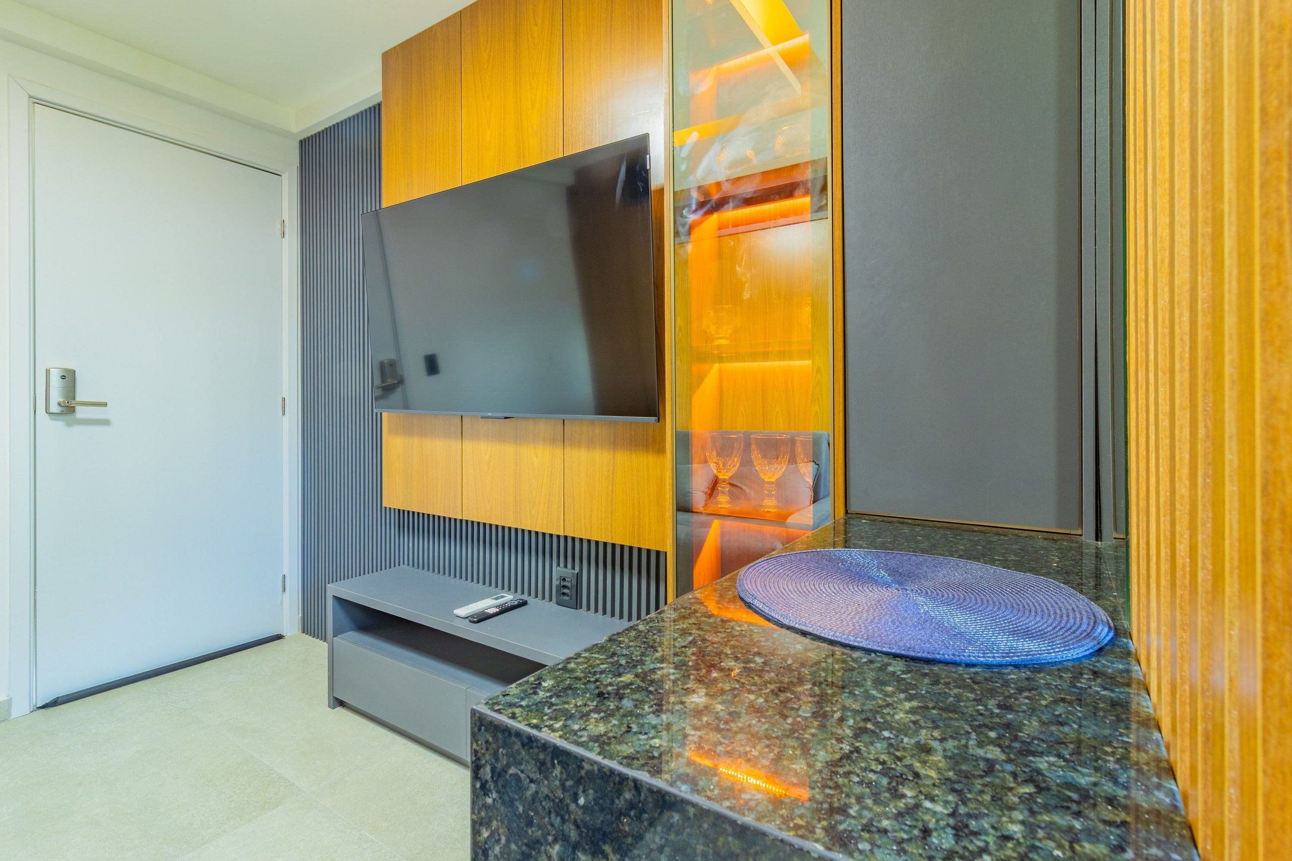 A modern bathroom with a granite countertop, a built-in TV, and wooden cabinetry.